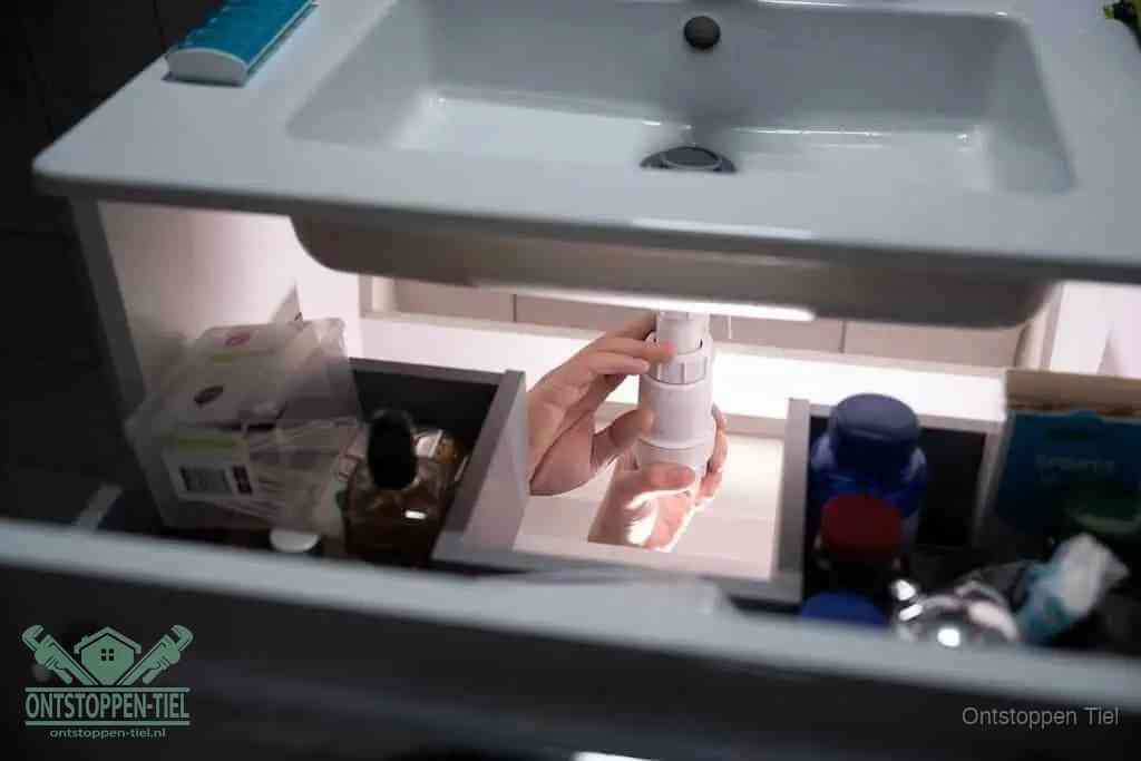 Een pompfles met zeep boven een wastafel, de heet water en afwasmiddel-methode om een vetprop in de afvoer los te maken in Tiel