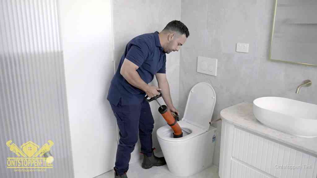 Een monteur buigt over een wandcloset en duwt met de hand een persluchtontstopper in de toiletpot om de verstopping handmatig los te maken in Tiel