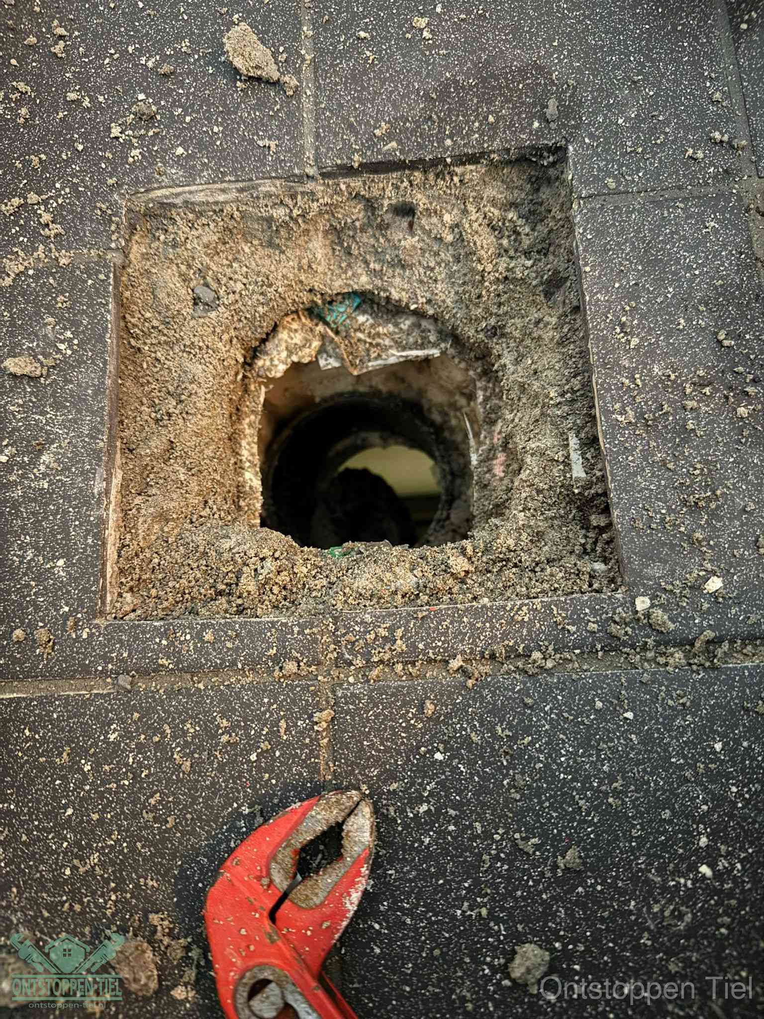 Een geopend rioolputje in een betontegelvloer met losgemaakt rooster en een zichtbare ronde afvoerbuis, het achterhalen waar de afvoerverstopping zit in Tiel