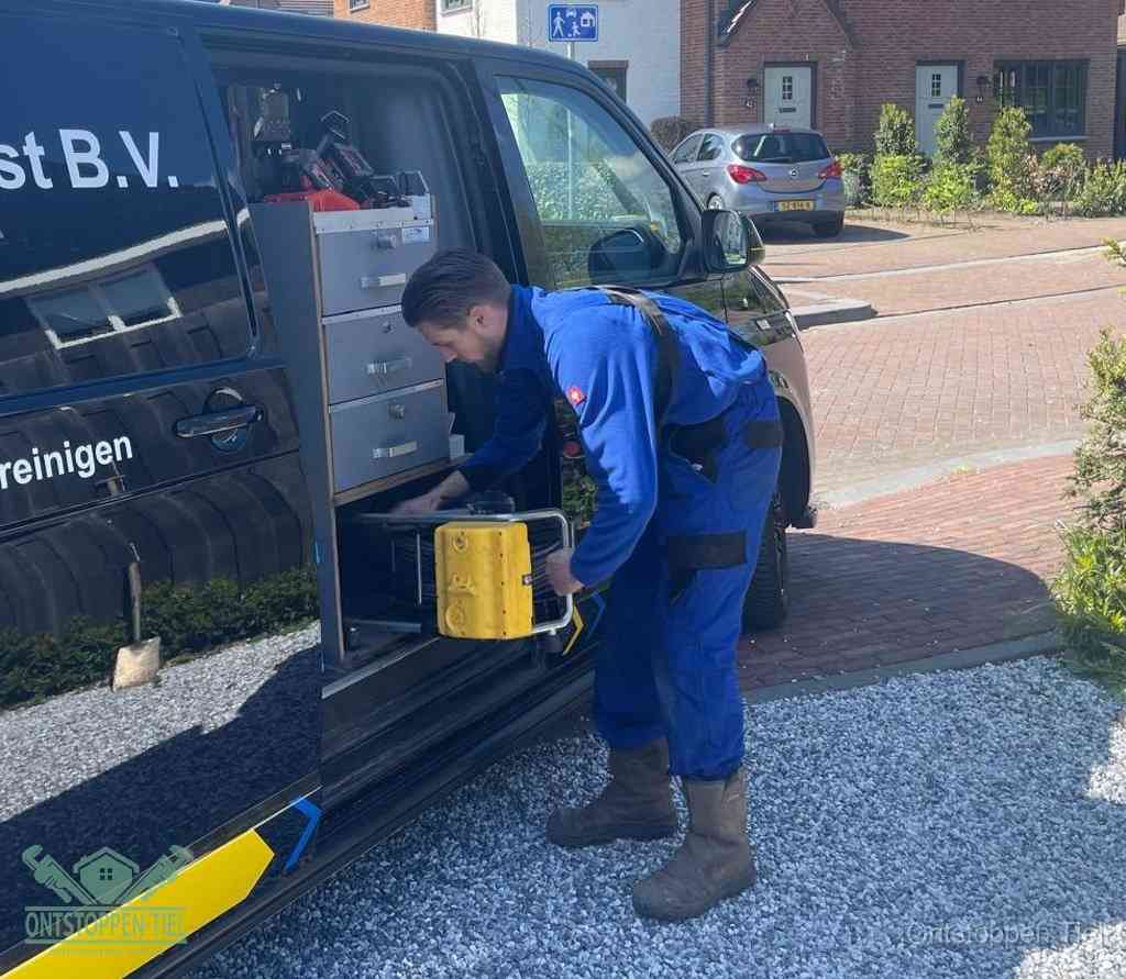 Een monteur pakt buiten op de oprit gereedschap uit de bedrijfsbus, het moment om een professional in te schakelen voor een verstopte afvoer in Tiel