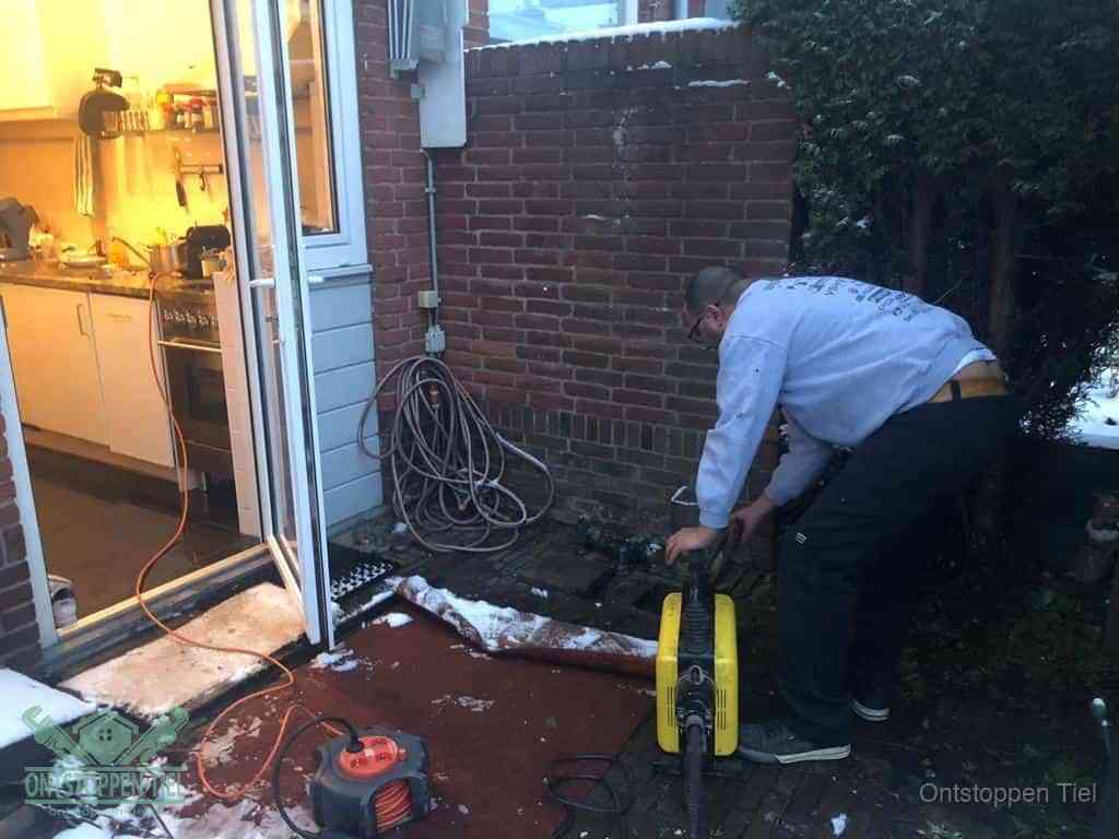 Een monteur werkt buiten bij een open riool-/grondput met een elektrische ontstoppingsmachine om een verborgen afvoerprobleem op te sporen in Tiel