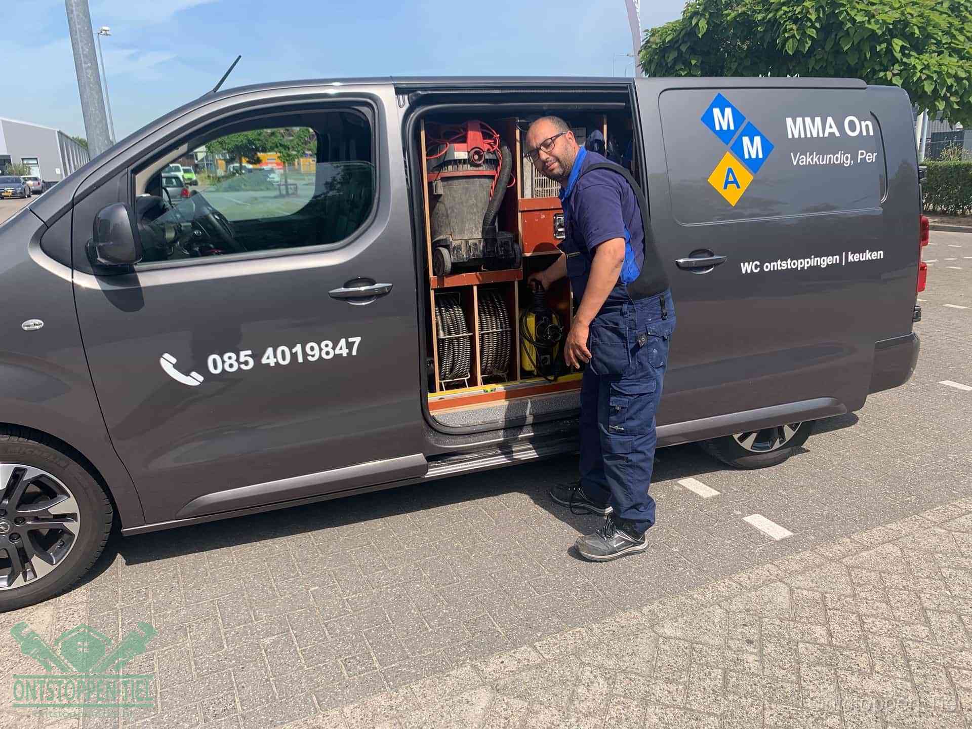 Een monteur bij de open schuifdeur van zijn bedrijfsbus op een parkeerplaats, klaar om de oorzaak van terugkerende afvoerverstoppingen aan te pakken in Tiel
