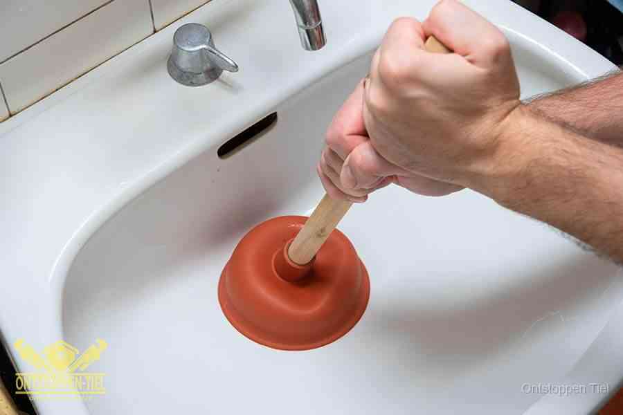 Twee handen gebruiken een rode rubberen plopper op een sanitair-afvoer om het toilet te ontstoppen in Tiel