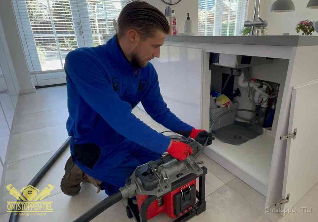 Een monteur voert een professionele elektrische ontstoppingsmachine in de afvoer onder de spoelbak tijdens het gootsteen ontstoppen in Tiel