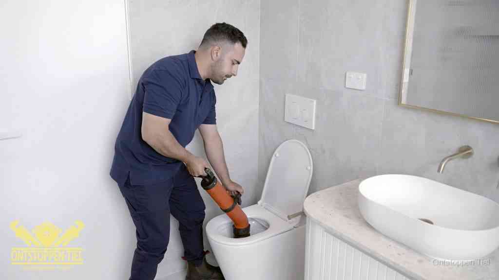 Een man gebruikt een handmatige luchtdruk-ontstopper in een modern betegeld toilet om zelf de wc te ontstoppen in Tiel